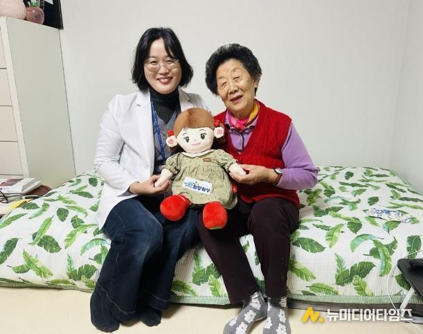 화성시동탄보건소 관계자와 독거 어르신이 AI 돌봄로봇 ‘효돌이’를 함께 들고 환하게 웃고 있다